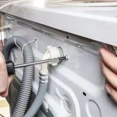 Ręce przykręcają śrubę przy przyłączu wody, co jest częścią instrukcji, jak podłączyć pralkę.
