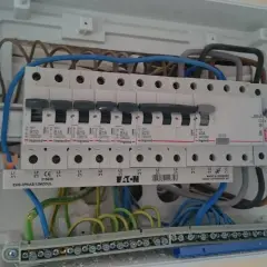 W skrzynce elektrycznej widać zabezpieczenie przedlicznikowe, bezpieczniki i przewody. Czerwona strzałka wskazuje śrubę mocującą szynę.