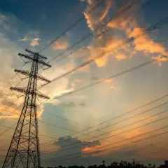 Wieże energetyczne na tle zachodzącego słońca, z chmurami w odcieniach pomarańczy i błękitu. THD.