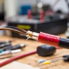 Przewody elektryczne z odsłoniętymi żyłami, owinięte taśmą izolacyjną. W tle widać sprzęt elektroniczny, co nie przewodzi prądu.