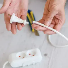 Dłonie przygotowują kabel do podłączenia do wtyczki z uziemieniem. W tle widać listwę zasilającą.