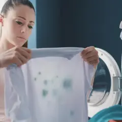 Kobieta z niedowierzaniem patrzy na poplamioną koszulkę, która wyszła z pralki.