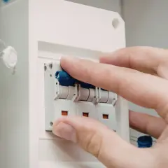 Dłoń manipuluje wyłącznikami w skrzynce elektrycznej. Dowiedz się, jak dobrać zabezpieczenie prądowe.