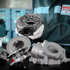 Mechanik w rękawiczkach prezentuje części turbosprężarki, w tym wirnik i obudowę. Na jego kombinezonie widnieje logo Bosch Service. P0299.