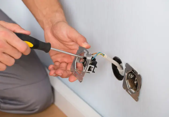 Elektryk dokonuje mostkowania gniazdka z bolcem, przykręcając mechanizm.