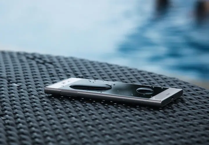 Smartfon z kroplami wody na ekranie, leżący na plecionej powierzchni. Dowód, że IP68 co oznacza: odporność na zanurzenie.