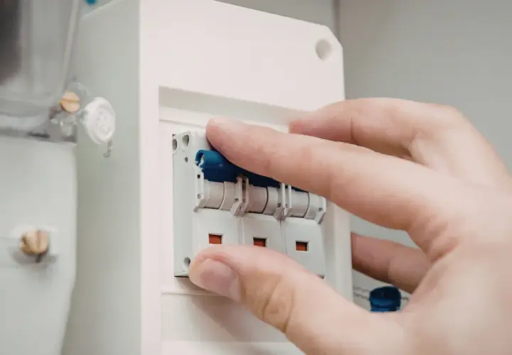 Dłoń manipuluje wyłącznikami w skrzynce elektrycznej. Dowiedz się, jak dobrać zabezpieczenie prądowe.