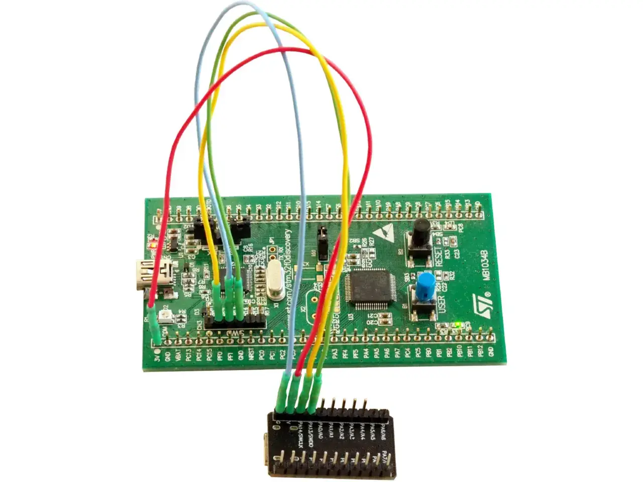Zielona płytka STM32 z kolorowymi przewodami podłączonymi do małego modułu.