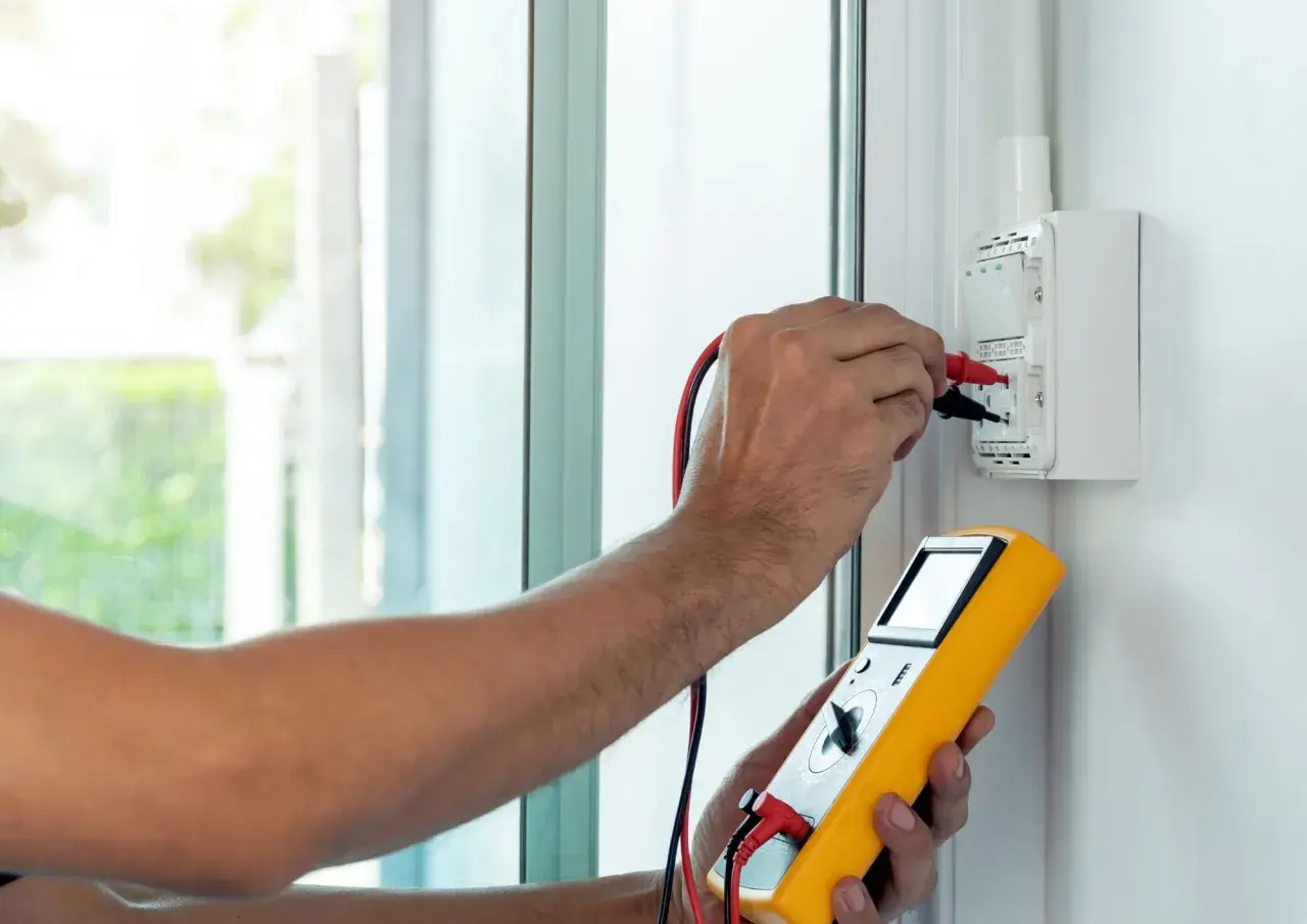 Elektryk wykonuje pomiar impedancji pętli zwarcia za pomocą żółtego miernika.