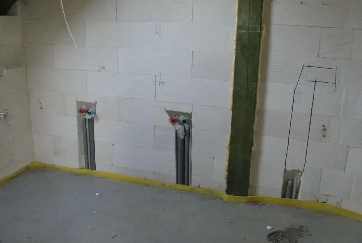 Ściana z bloczków z widocznymi bruzdami pod kable i instalacją wodną. Przygotowania do montażu elektryki i hydrauliki.